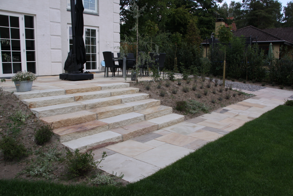 Terrasse med niveauforskelle: Terrasse i flere niveauer med sandstenstrin, der skaber dynamik og struktur i haven.