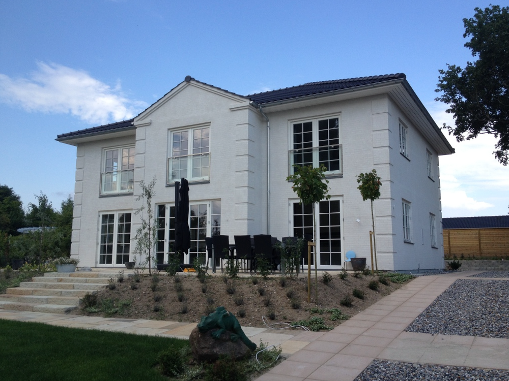 Grøn forhave med moderne design: Velplejet have med græsplæne og moderne elementer, der harmonerer med ejendommen.